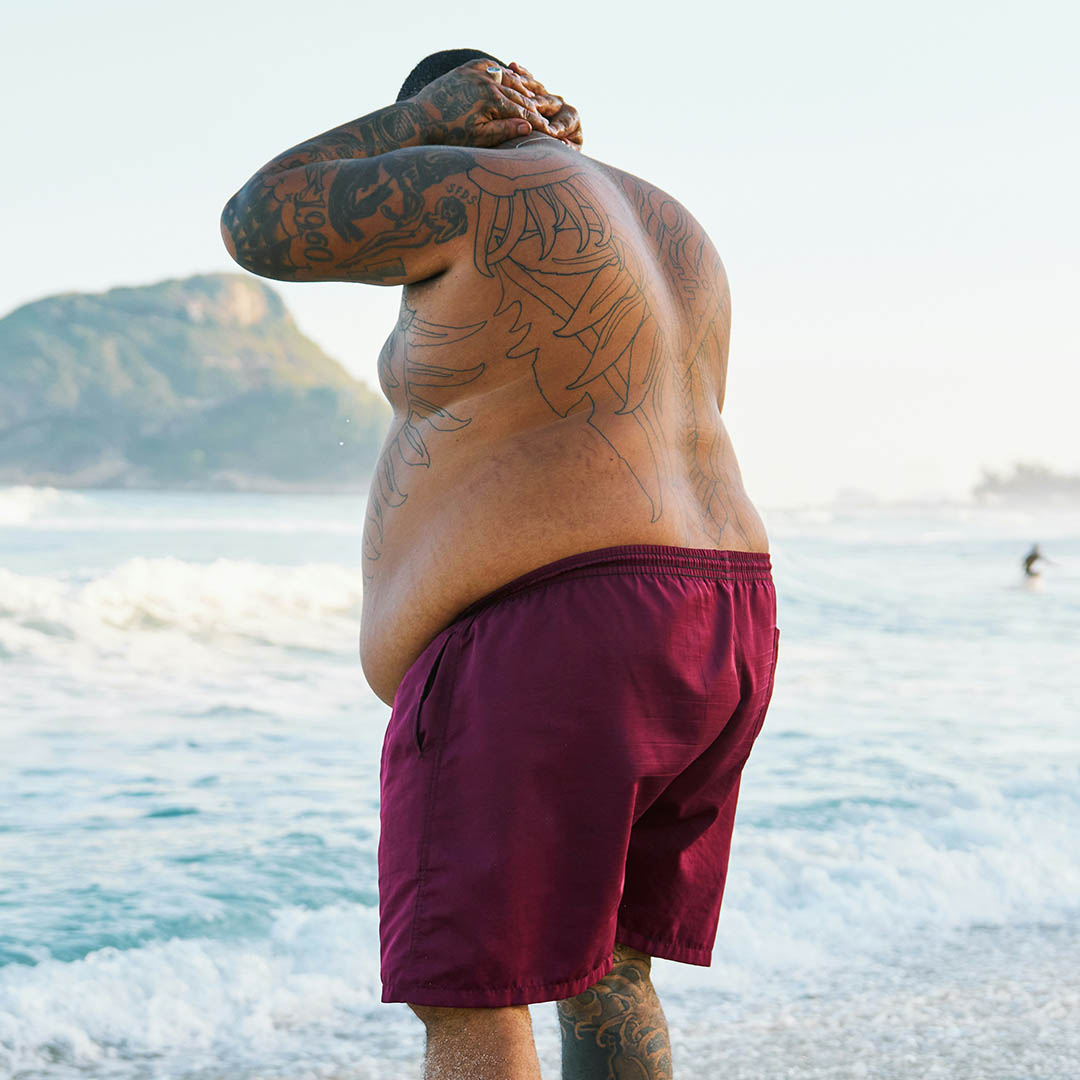 Tattooed man shirtless at beach, showing torso and back from behind